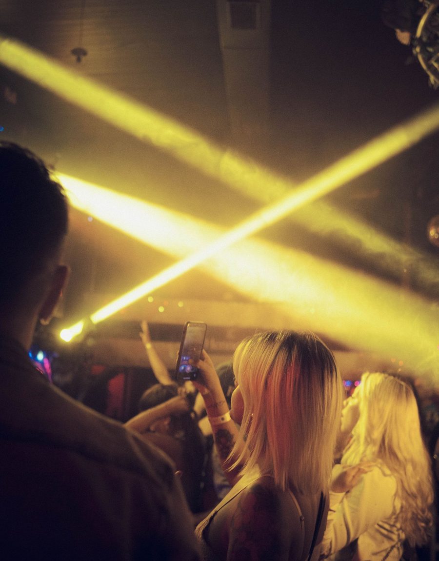 A crowd lit up under bright crossing yellow club light beams