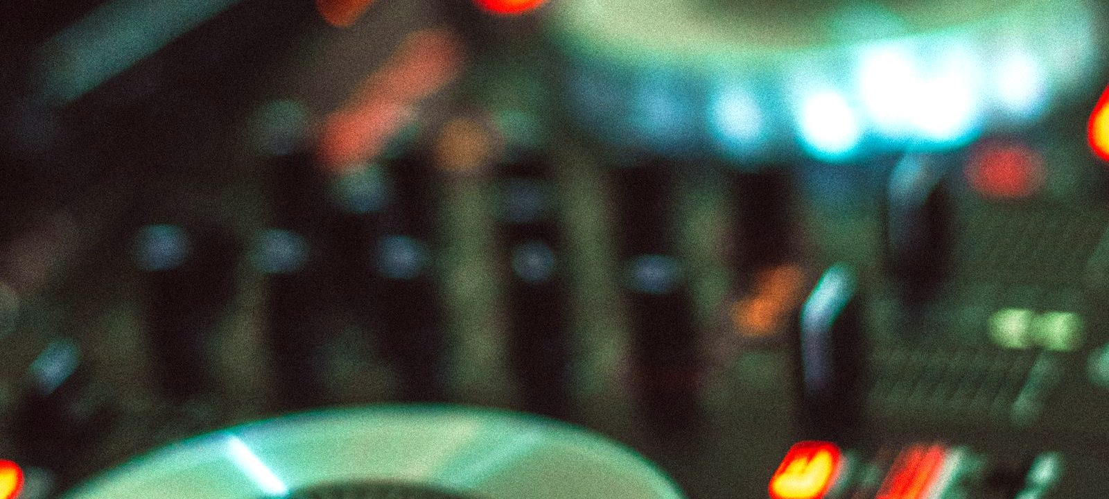 Two glowing jog wheels and channel faders on a DJ setup lit in warm and blue light