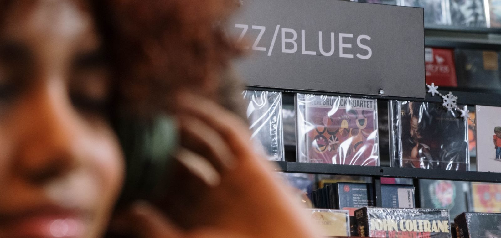 A DJ listening intently through one ear cup of their headphones, surrounded by records